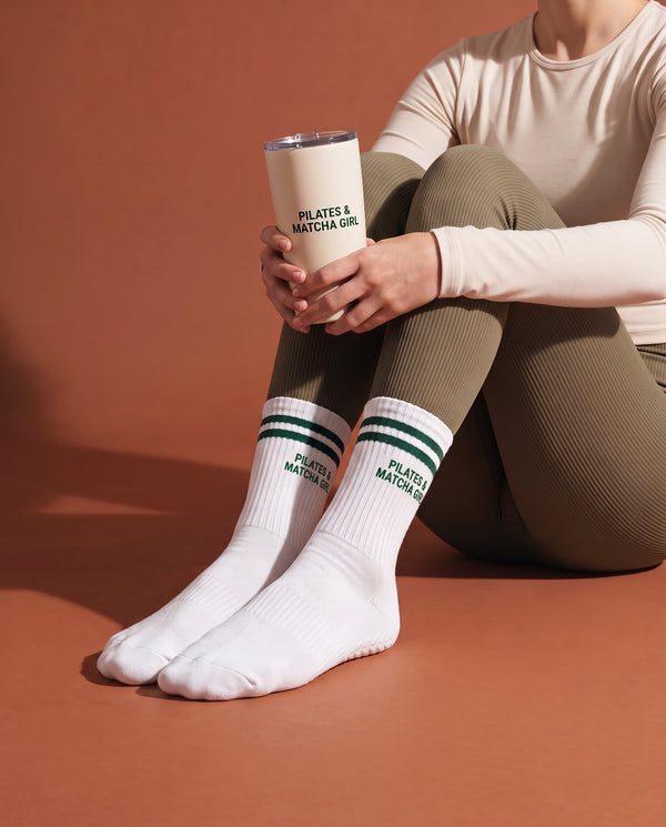 Caixa de oferta Pilates & Matcha: sentada no chão, caneca Pilates & Matcha Girl e meias Maison Matcha, estúdio terracota