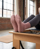 Semelles des chaussettes Dusty Rose appuyées sur la barre d'un reformer, picots de grip apparents