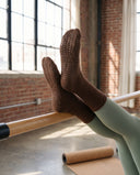 Pieds chaussés d'Espresso posés sur la barre en bois d'un reformer, talon renforcé visible