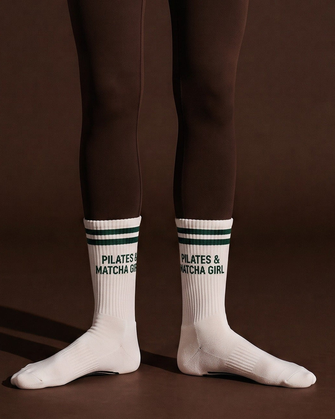 Polar Star x Maison Matcha: białe skarpetki do pilatesu do połowy łydki w zielone paski, na stopach na stojąco, zbliżenie, brązowe tło